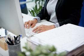 Frau, die am Schreibtisch im Büro sitzt und auf einer Tastatur schreibt