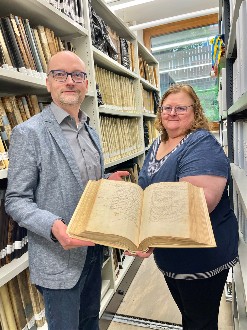 Die Stadtarchivare halten im Archiv ein Buch von 1564 in Händen.